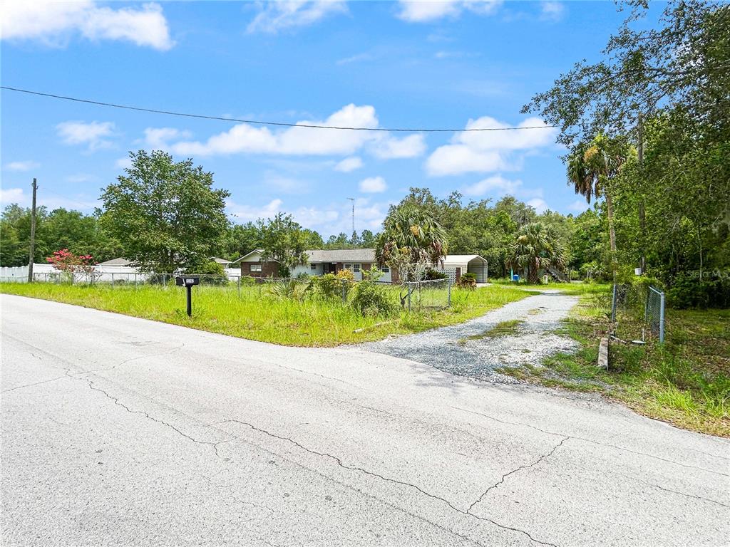 A single-story house with a gravel driveway sits on a grassy lot near a road — 23162 SW NEPTUNE BOULEVARD, DUNNELLON, FL