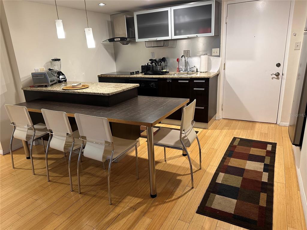 A kitchen features dark cabinets, granite countertops, a dining table with chairs, and wood flooring — 701 S MADISON AVENUE UNIT 410, CLEARWATER, FL
