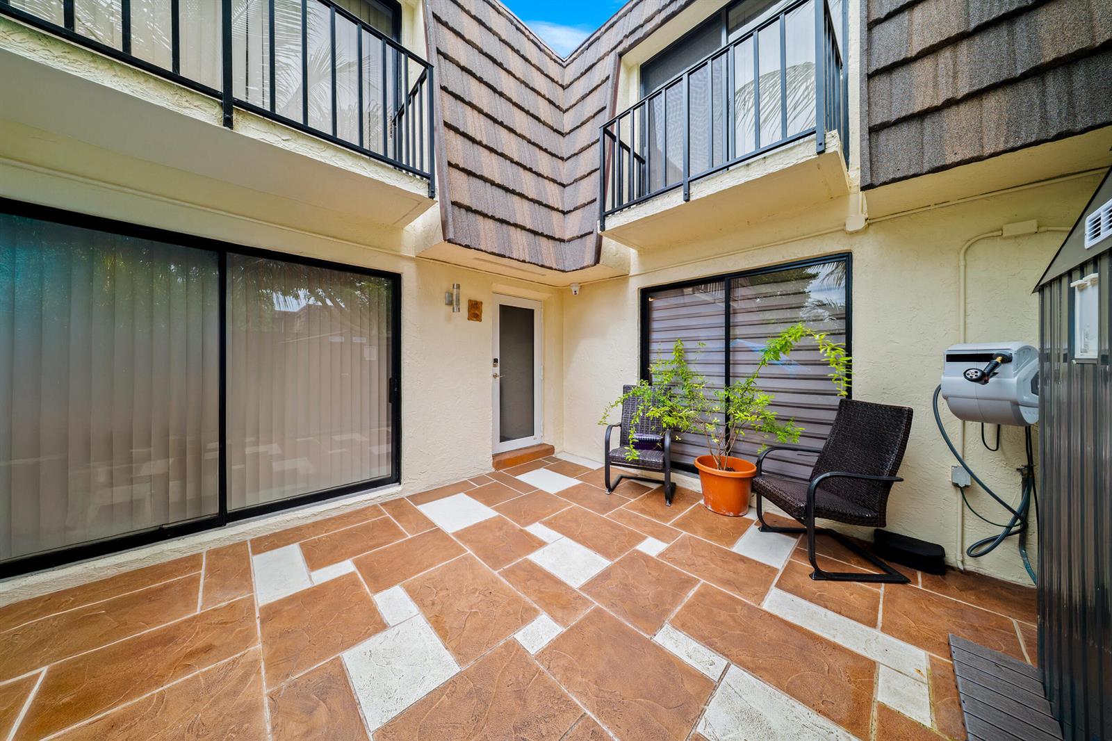 A paved patio area features two chairs, a potted plant, and sliding glass doors — 1524 Forest Lakes Circle, West Palm Beach FL 33406, WEST PALM BEACH, FL