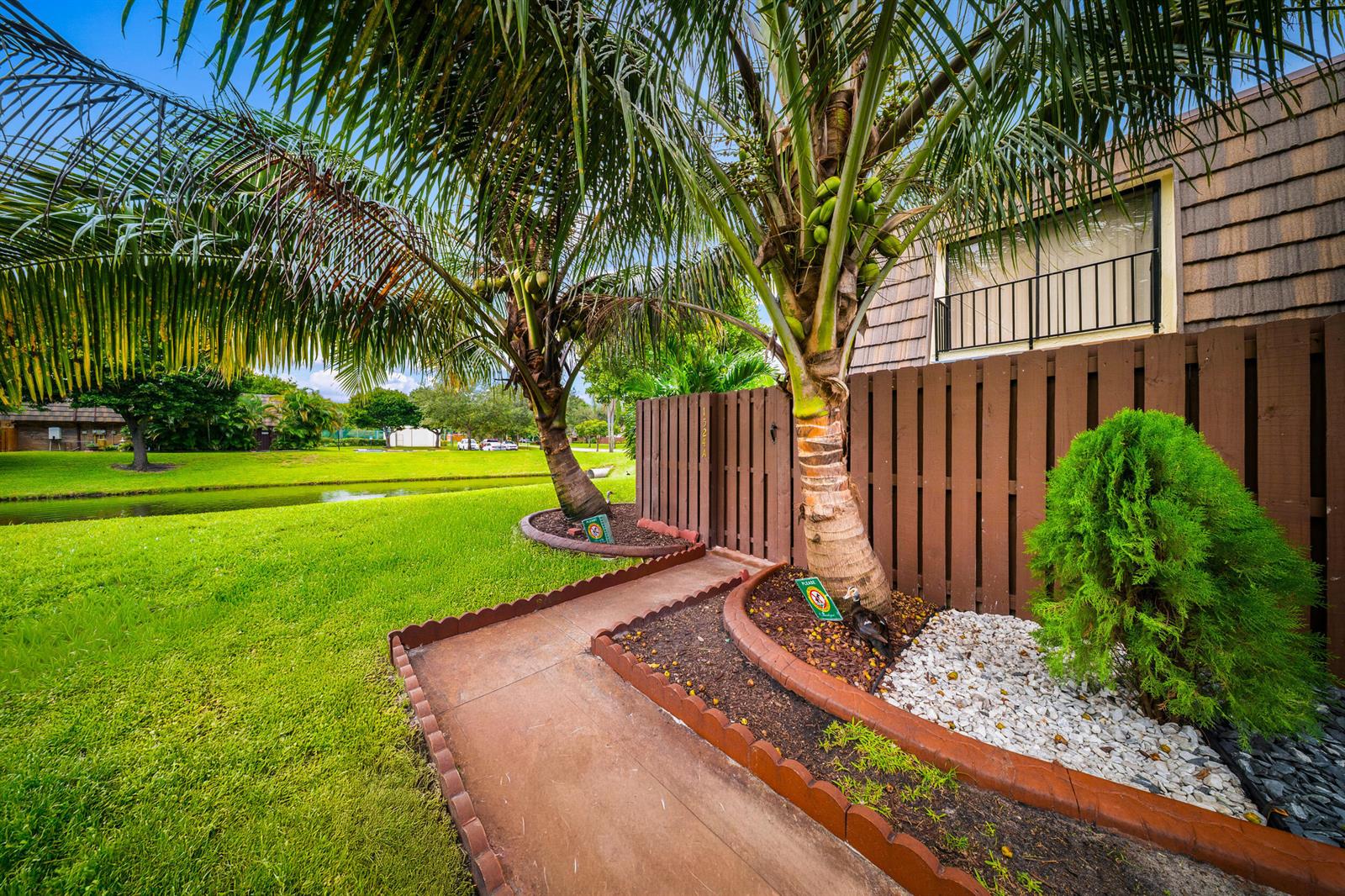 A concrete walkway leads to a wooden gate beside a palm tree and green lawn — 1524 Forest Lakes Circle, West Palm Beach FL 33406, WEST PALM BEACH, FL