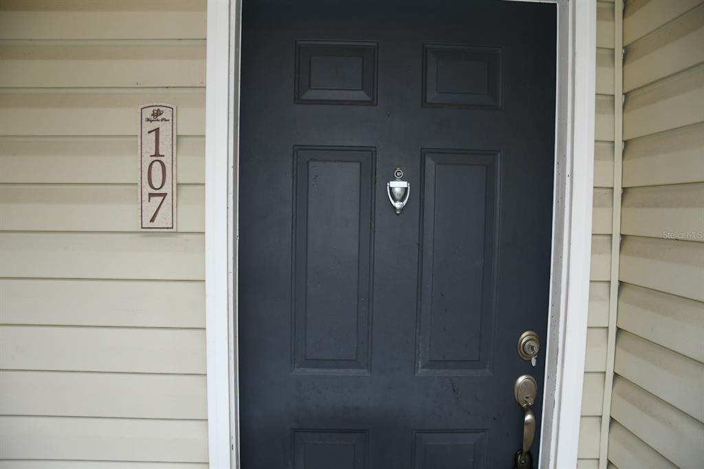 A dark gray front door with a silver knocker and handle sits beside a house number — 5062 NW 44TH LANE UNIT 107, GAINESVILLE, FL