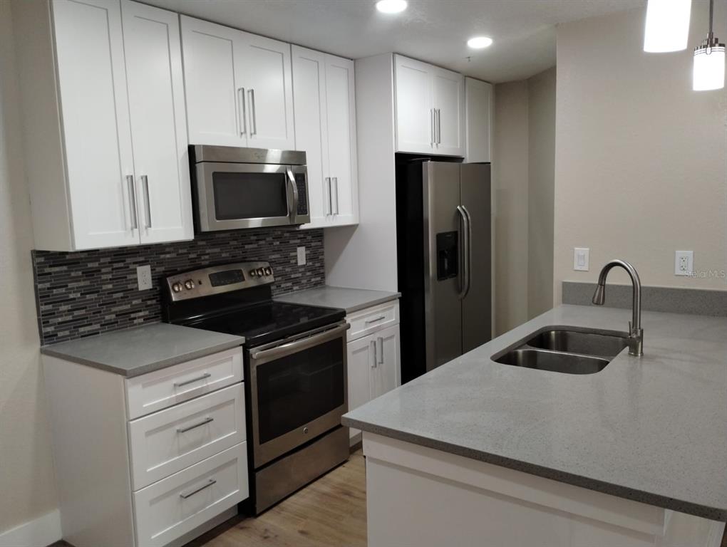A modern kitchen features white cabinets, stainless steel appliances, gray countertops, and a tiled backsplash — 623 DORY LANE UNIT 306, ALTAMONTE SPRINGS, FL