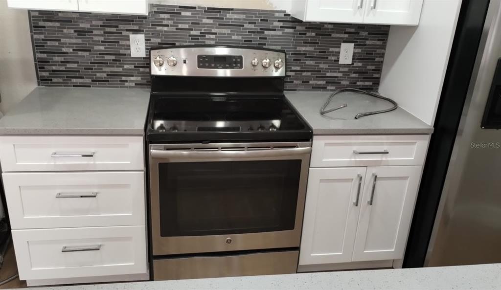 A kitchen features a stainless steel electric range, white cabinets, and a gray tiled backsplash — 623 DORY LANE UNIT 306, ALTAMONTE SPRINGS, FL