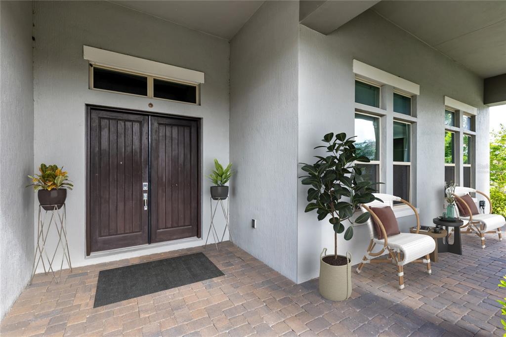 A covered front porch features a double wooden door, brick pavers, and outdoor seating — 13370 ALDERLEY DRIVE, ORLANDO, FL