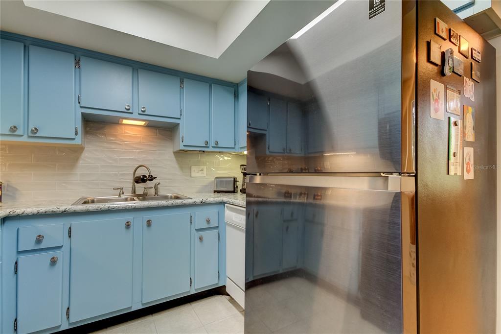 A kitchen features blue cabinets, a stainless steel refrigerator, and a white subway tile backsplash — 9537 86TH AVENUE UNIT 9537, SEMINOLE, FL