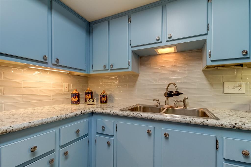 A kitchen features light blue cabinets, a white granite countertop, and a subway tile backsplash — 9537 86TH AVENUE UNIT 9537, SEMINOLE, FL
