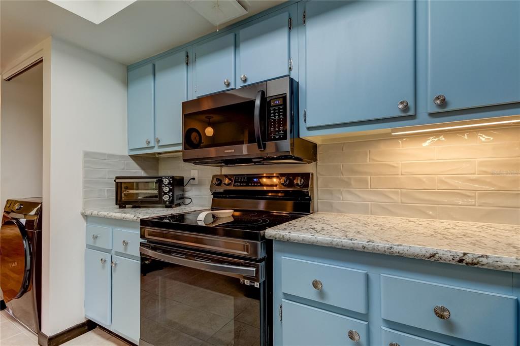A kitchen features blue cabinets, granite countertops, a black stove, and a subway tile backsplash — 9537 86TH AVENUE UNIT 9537, SEMINOLE, FL