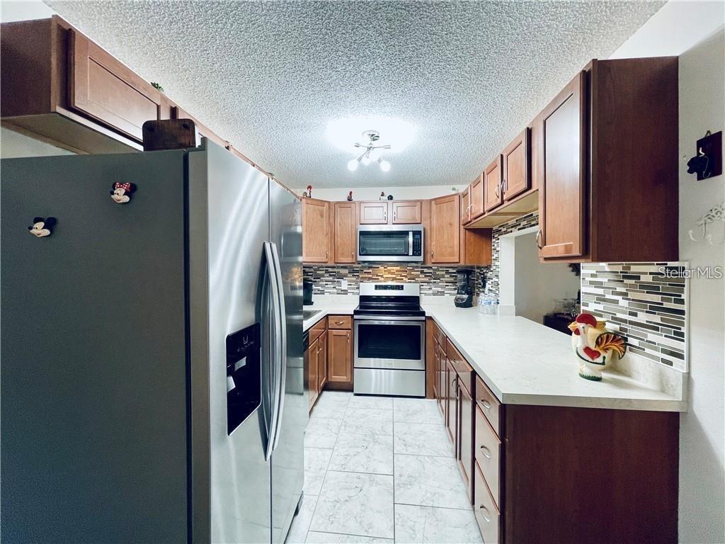 A galley kitchen features wood cabinets, stainless steel appliances, and a tiled backsplash — 1723 PINE RIDGE ROAD UNIT 23, SANFORD, FL