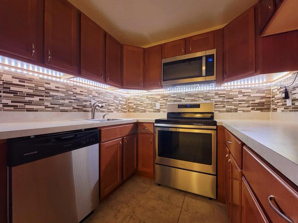 A kitchen with wood cabinets, stainless steel appliances, and a tiled backsplash with under-cabinet lighting — 1723 PINE RIDGE ROAD UNIT 23, SANFORD, FL