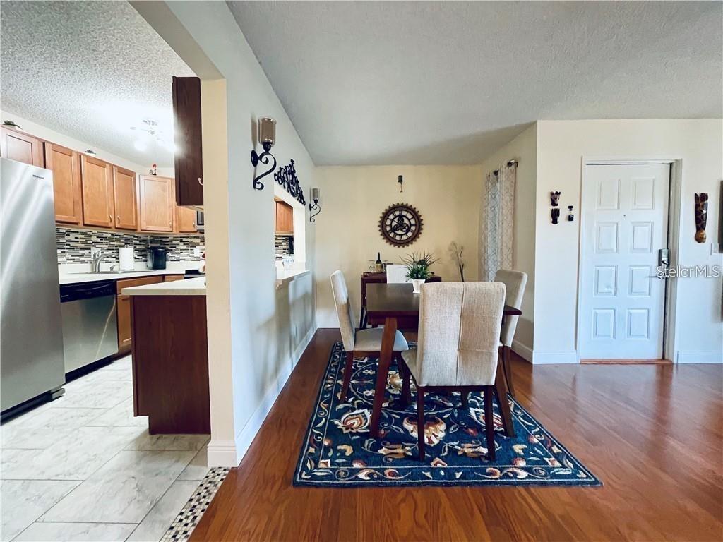 A dining area with a patterned rug sits adjacent to a kitchen with wooden cabinets — 1723 PINE RIDGE ROAD UNIT 23, SANFORD, FL