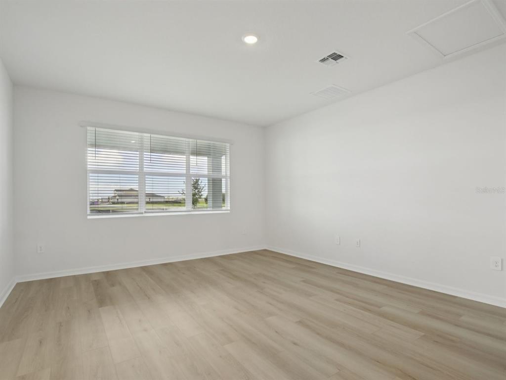 An empty room with light wood-look flooring, white walls, and a large window with blinds — 13213 SHELLMORE AVENUE, PALMETTO, FL