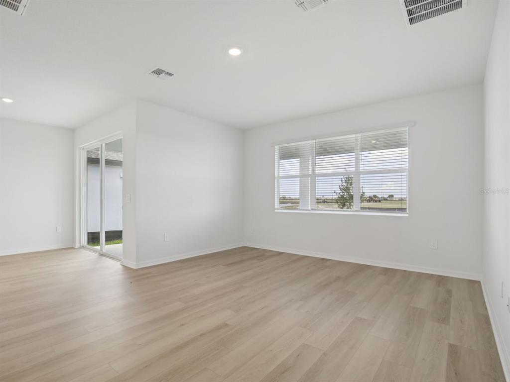 An empty room with light wood-look flooring, white walls, a large window, and sliding doors — 13213 SHELLMORE AVENUE, PALMETTO, FL
