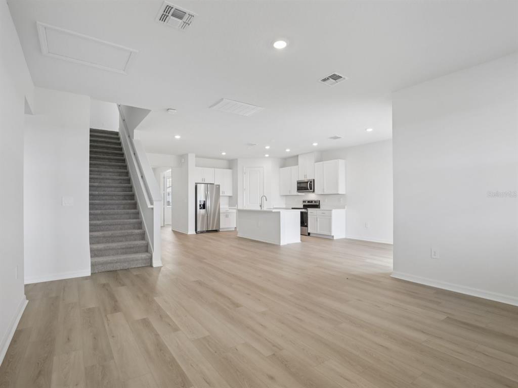 An open-concept kitchen and living area features light wood flooring and a carpeted staircase — 13213 SHELLMORE AVENUE, PALMETTO, FL