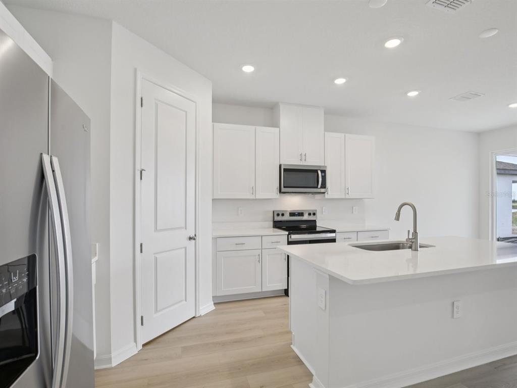 A modern kitchen features white cabinets, stainless steel appliances, and a central island with sink — 13213 SHELLMORE AVENUE, PALMETTO, FL