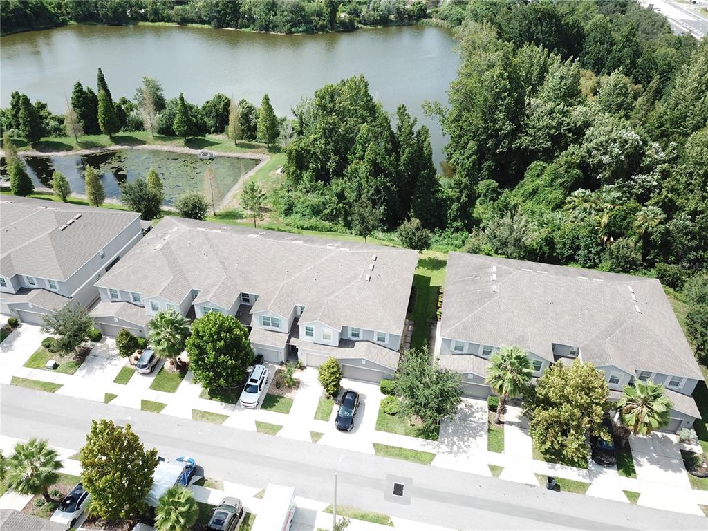 An aerial view shows townhouses with gray roofs situated next to a lake and trees — 10676 LAKE MONTAUK DRIVE, RIVERVIEW, FL