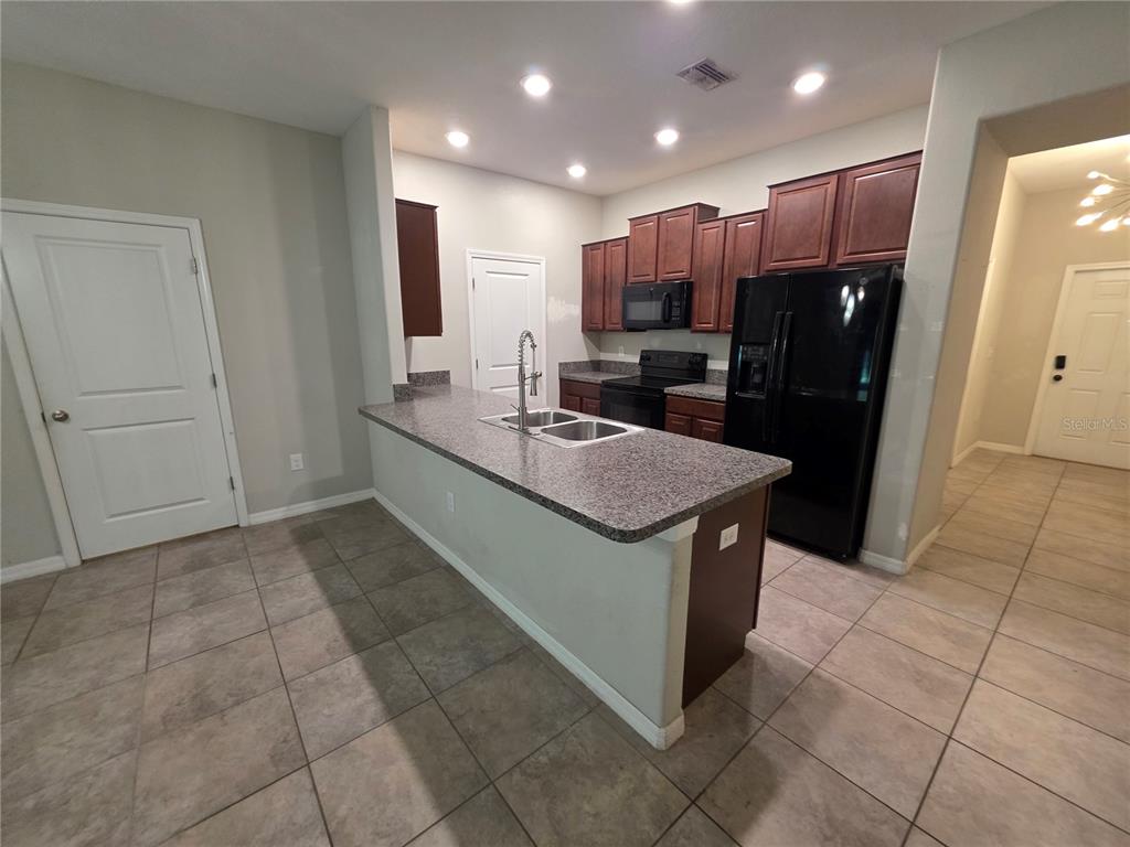 A kitchen with dark wood cabinets, black appliances, and a granite-topped island with a sink — 10676 LAKE MONTAUK DRIVE, RIVERVIEW, FL