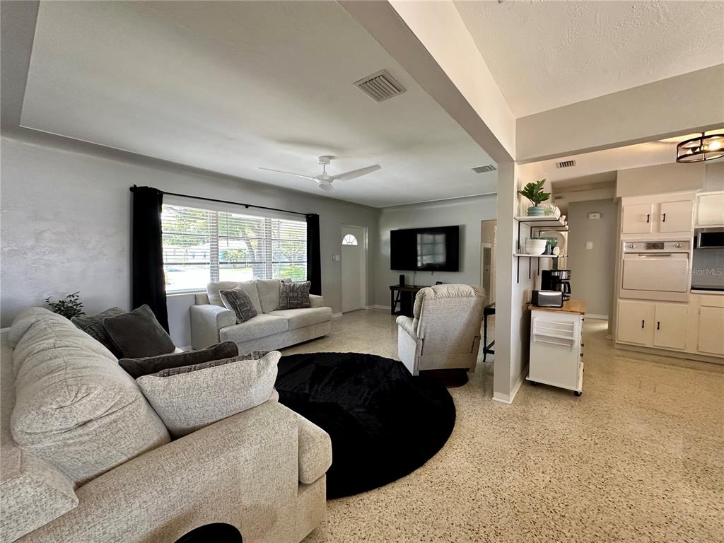 A living room with light-colored sofas, a circular rug, and an adjacent kitchen area — 4917 99TH STREET N, ST PETERSBURG, FL