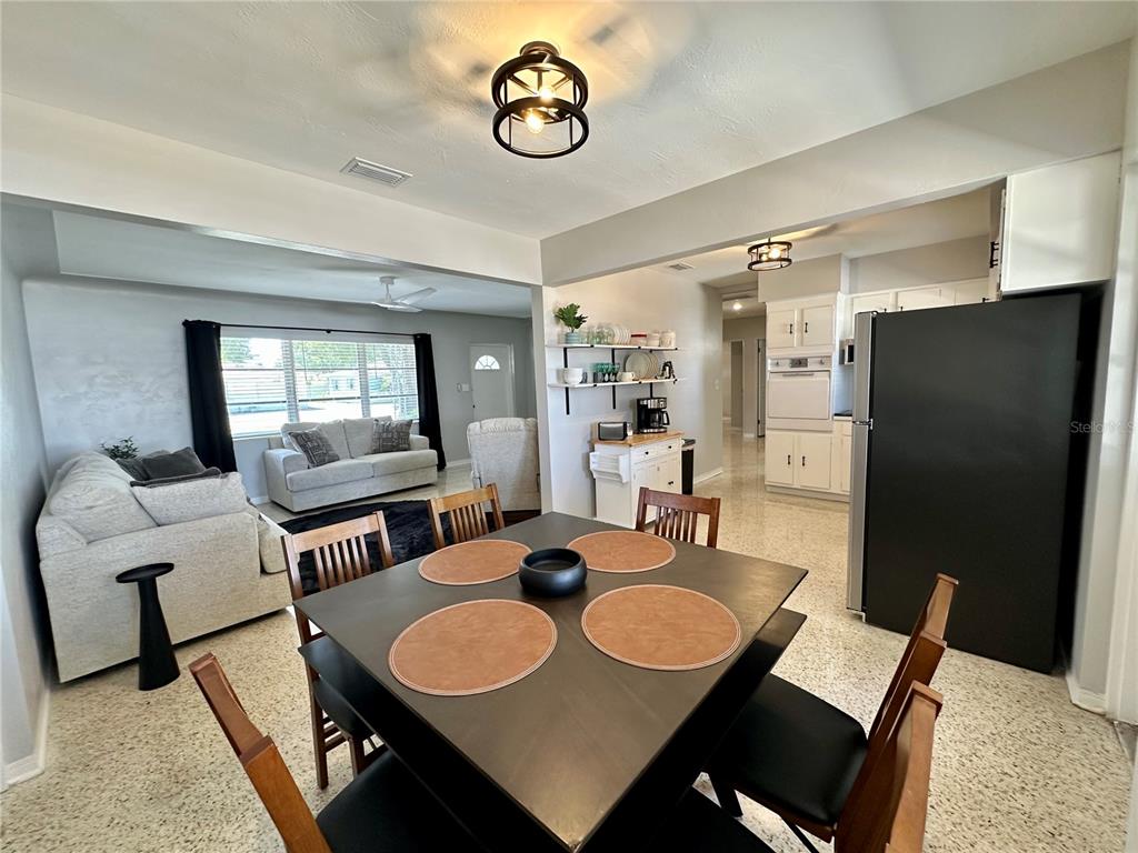 A dining area with a dark square table opens into a living room and kitchen — 4917 99TH STREET N, ST PETERSBURG, FL