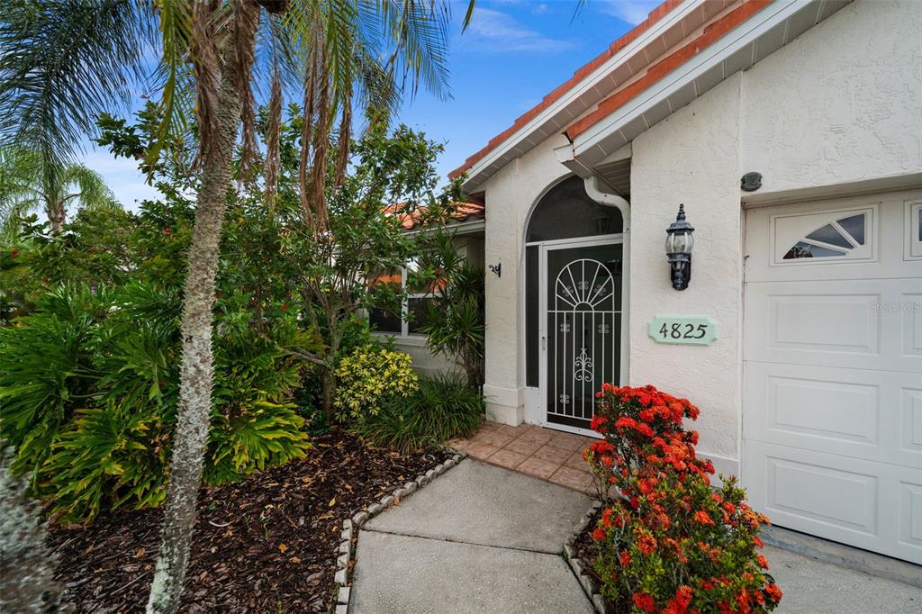 The exterior of a house features a white stucco wall, a tiled roof, and landscaping — 4825 TAMARACK TRAIL, VENICE, FL
