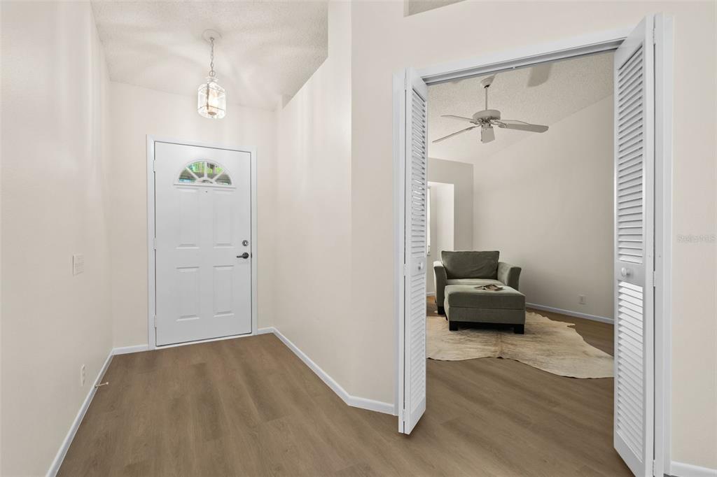 An entryway with light wood-look flooring leads to a room with a chair and ottoman — 4825 TAMARACK TRAIL, VENICE, FL