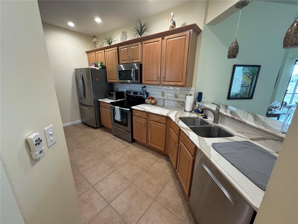 A kitchen features wood cabinets, stainless steel appliances, and light-colored countertops with a tile floor — 20096 PEZZANA DRIVE, VENICE, FL