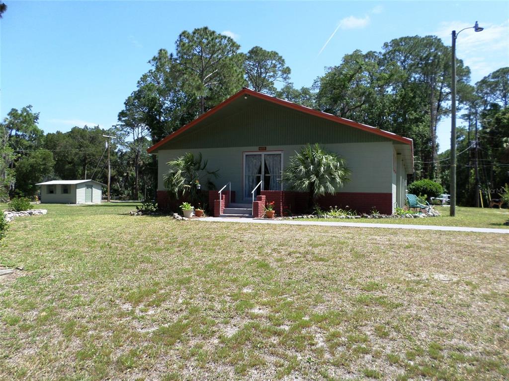 A single-story building with a green facade, red brick base, and a detached shed nearby — 6005 HIGHWAY 40 W, YANKEETOWN, FL