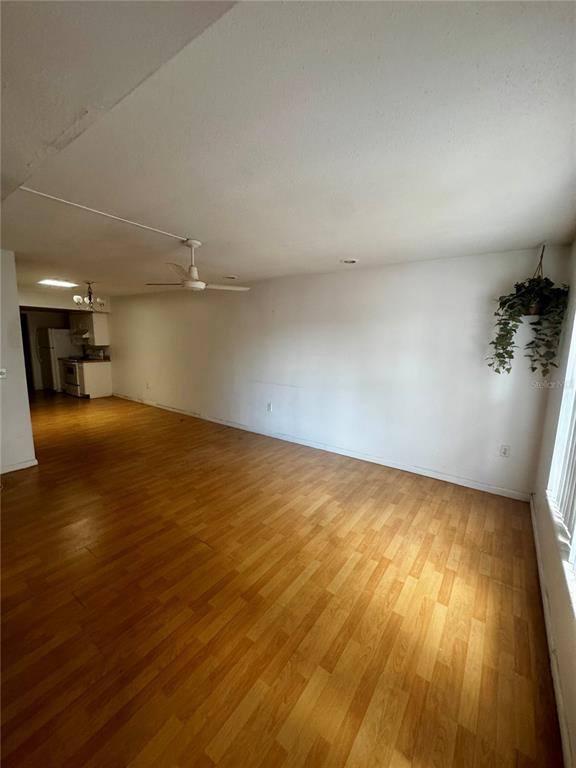 An empty living room with wood-look flooring, a ceiling fan, and a view into the kitchen — 2929 W OAK RIDGE ROAD UNIT F4, ORLANDO, FL