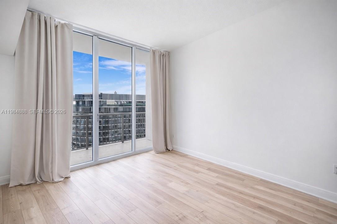 An empty room features light wood flooring, white walls, and floor-to-ceiling windows with curtains — 1750 N Bayshore Dr # 3811, Miami FL 33132, MIAMI, FL