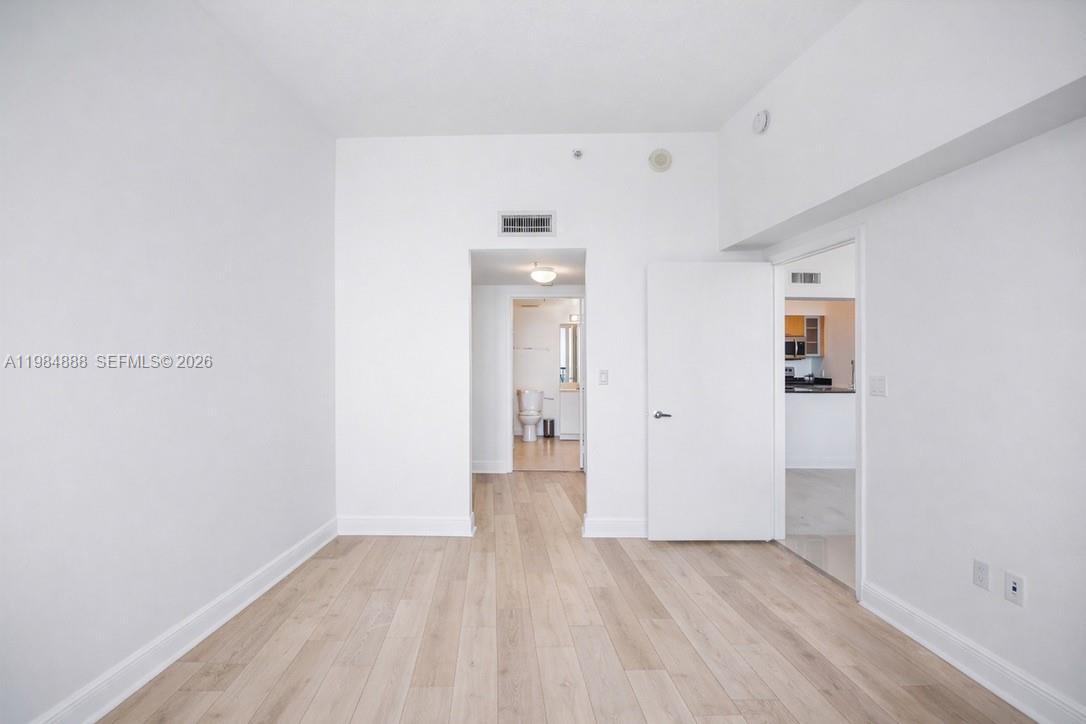 An empty room with light wood-look flooring, white walls, and doorways leading to other areas — 1750 N Bayshore Dr # 3811, Miami FL 33132, MIAMI, FL