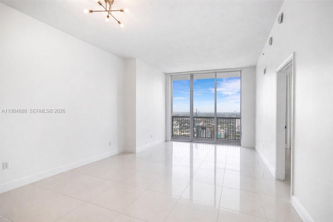 A bright, empty room features white walls, large floor-to-ceiling windows, and light-colored tile flooring — 1750 N Bayshore Dr # 3811, Miami FL 33132, MIAMI, FL