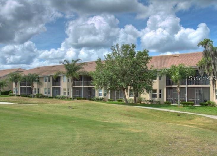 A multi-story apartment building with screened balconies overlooks a grassy golf course — 803 FAIRWAYCOVE LANE UNIT 204, BRADENTON, FL