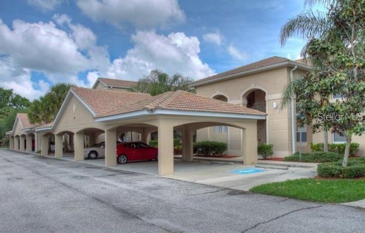 A beige apartment building features a covered parking area with arched openings and tiled roofs — 803 FAIRWAYCOVE LANE UNIT 204, BRADENTON, FL