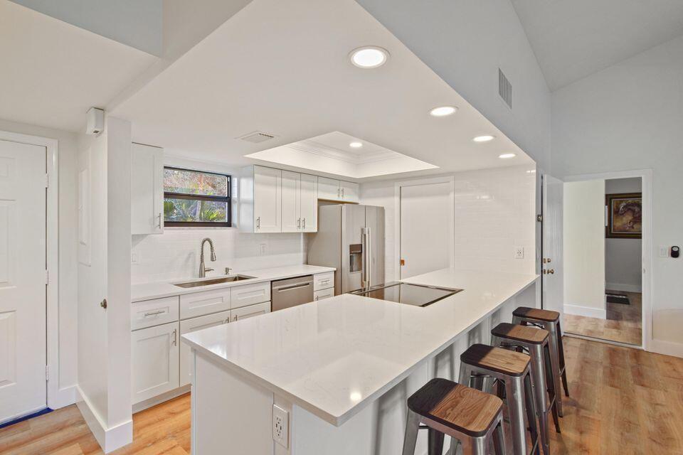 A modern kitchen features white cabinetry, quartz countertops, a large island, and stainless steel appliances — 11863 Wimbledon Circle # 509, Wellington FL 33414, WELLINGTON, FL