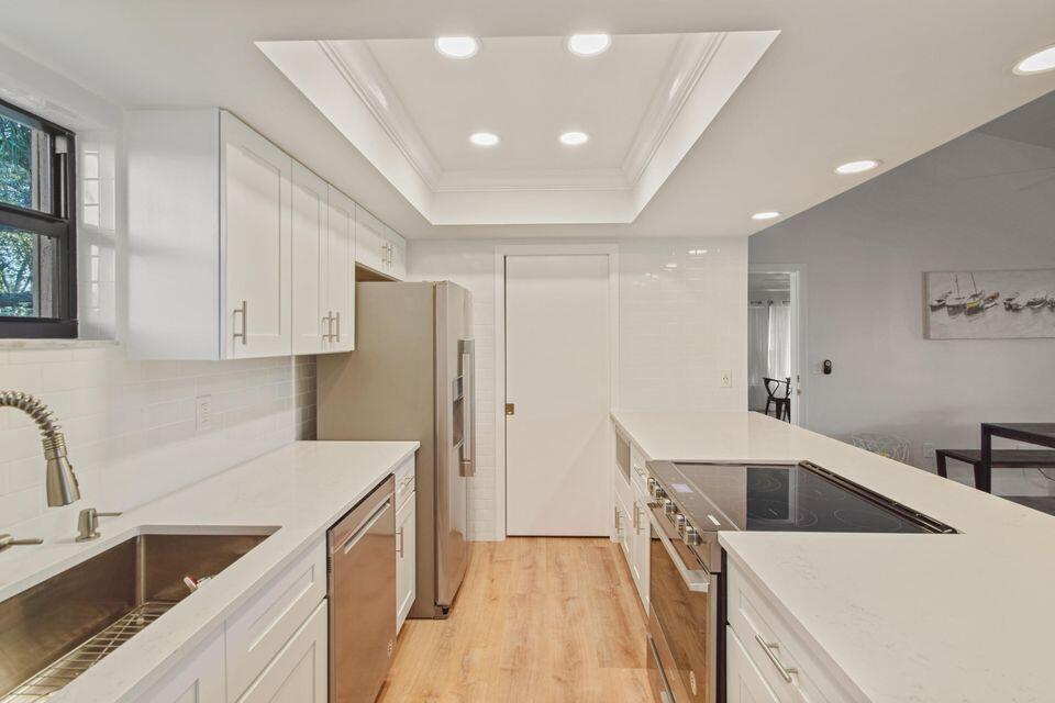 A modern kitchen features white cabinetry, stainless steel appliances, quartz countertops, and a tray ceiling — 11863 Wimbledon Circle # 509, Wellington FL 33414, WELLINGTON, FL