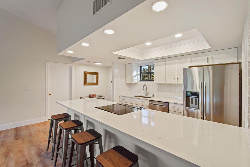 A modern kitchen features white cabinetry, stainless steel appliances, and a large quartz-topped island — 11863 Wimbledon Circle # 509, Wellington FL 33414, WELLINGTON, FL