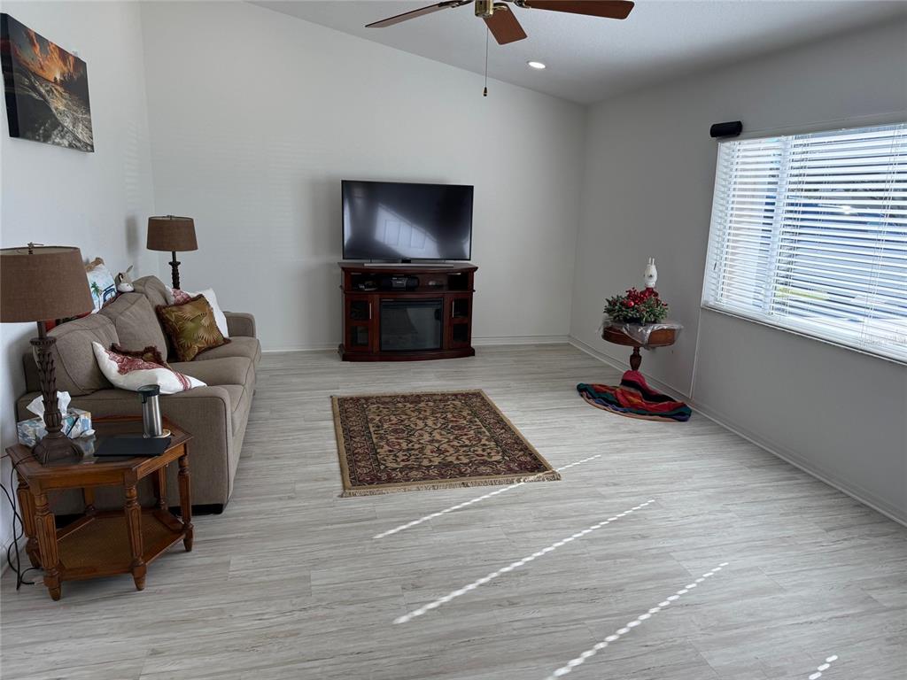 A living room features light wood-look flooring, a beige sofa, and a television on a stand — 9685 SE 136TH PLACE, SUMMERFIELD, FL