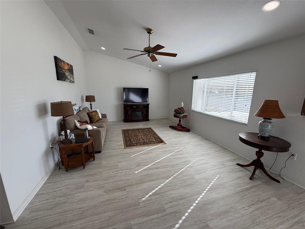 A living room features light wood-look flooring, a ceiling fan, and a large window — 9685 SE 136TH PLACE, SUMMERFIELD, FL