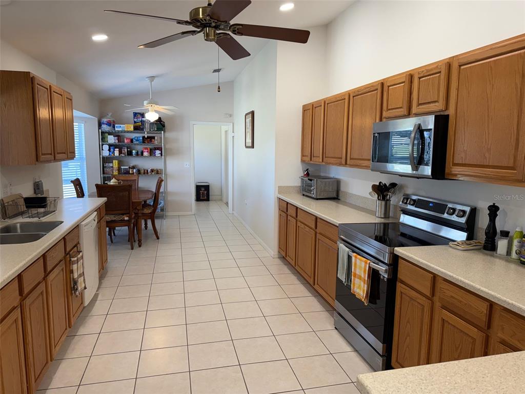 A kitchen features oak cabinets, stainless steel appliances, and light tile flooring — 9685 SE 136TH PLACE, SUMMERFIELD, FL