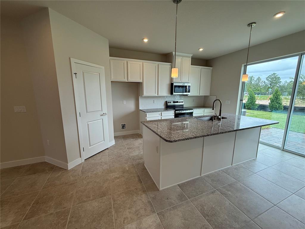 A kitchen features white cabinets, granite countertops, a center island, and a sliding glass door — 1229 PINEYWOOD FIELD DRIVE, DAVENPORT, FL