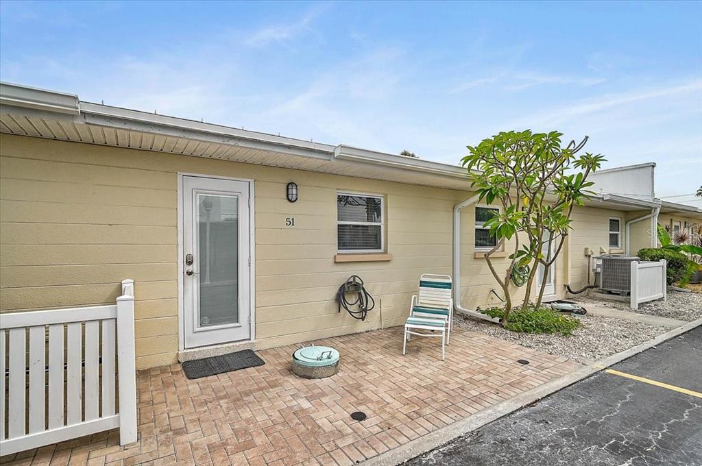 A beige single-story building exterior features a brick patio, a white door, and a chair — 5830 MIDNIGHT PASS ROAD UNIT 51, SARASOTA, FL