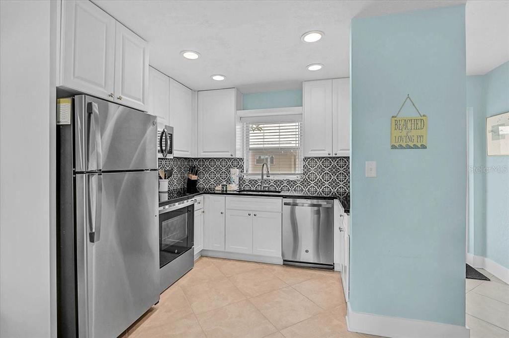 A kitchen features white cabinets, stainless steel appliances, black countertops, and a patterned tile backsplash — 5830 MIDNIGHT PASS ROAD UNIT 51, SARASOTA, FL