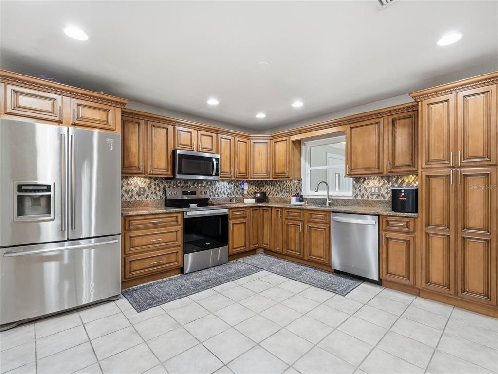 A kitchen features wood cabinets, stainless steel appliances, granite countertops, and light-colored tile flooring — 955 TIMBERGREEN DRIVE, LAKELAND, FL