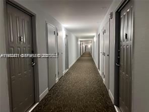 A long, narrow apartment hallway with gray doors and patterned carpet flooring — 200 Leslie Dr # 303, Hallandale Beach FL 33009, HALLANDALE BEACH, FL