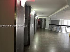 A hallway with grey tiled floors leads toward an elevator bank and a glass railing — 200 Leslie Dr # 303, Hallandale Beach FL 33009, HALLANDALE BEACH, FL