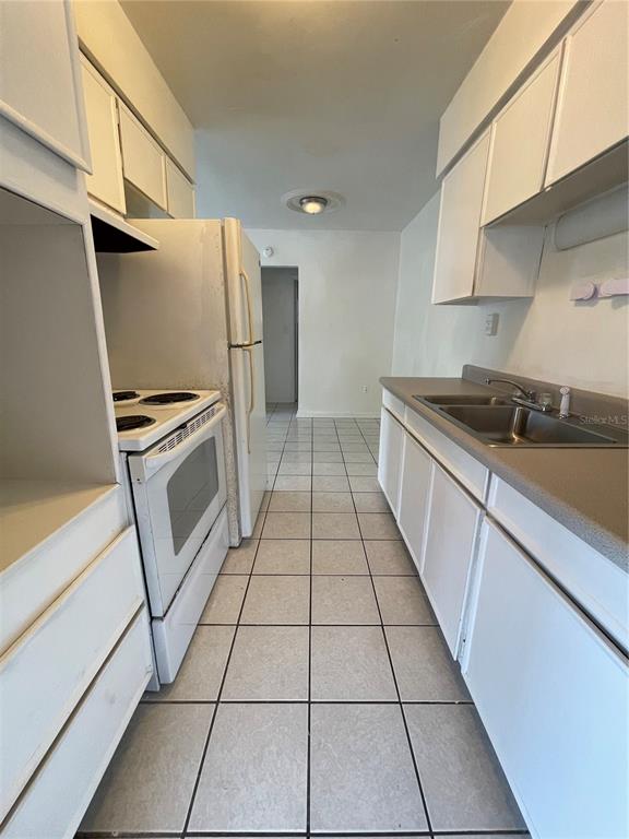 A galley kitchen features white cabinets, a white stove, a refrigerator, and light-colored tile flooring — 1600 INDIANA AVENUE, WINTER PARK, FL