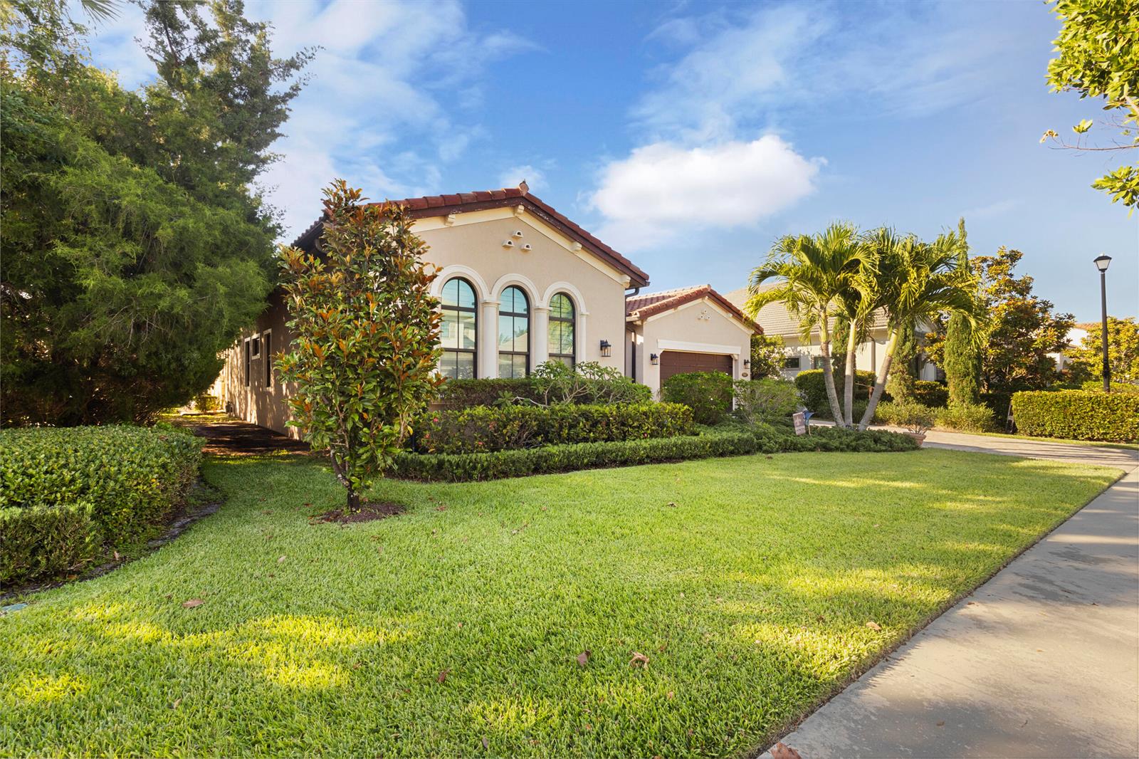 A single-story house with a tan stucco exterior, arched windows, and a manicured lawn — 9387 Grand Prix Lane, Boynton Beach FL 33472, BOYNTON BEACH, FL