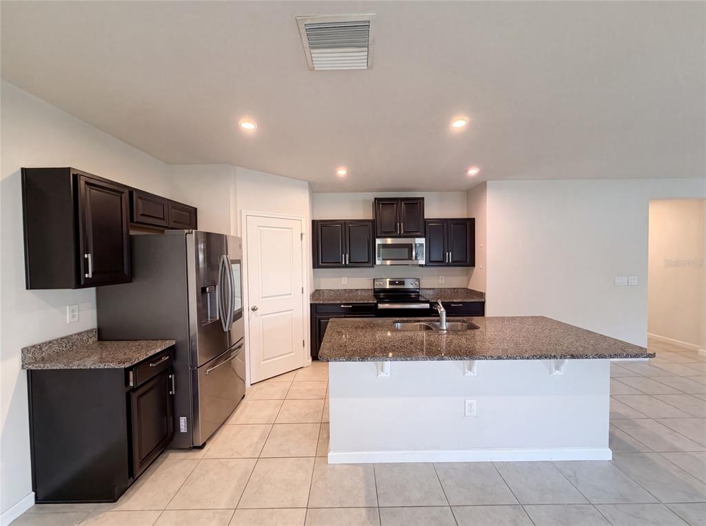A kitchen features dark wood cabinets, granite countertops, stainless steel appliances, and a central island — 10654 HAWKS LANDING DRIVE, LAND O LAKES, FL