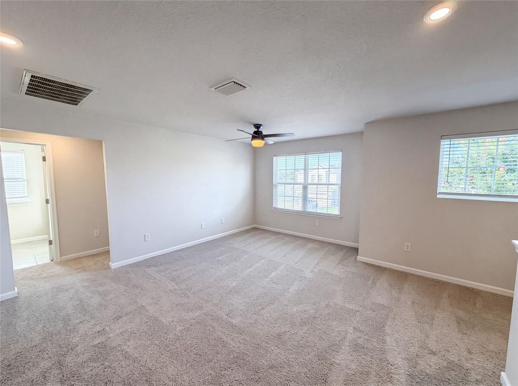 An empty room features beige carpeting, light-colored walls, a ceiling fan, and two windows — 10654 HAWKS LANDING DRIVE, LAND O LAKES, FL