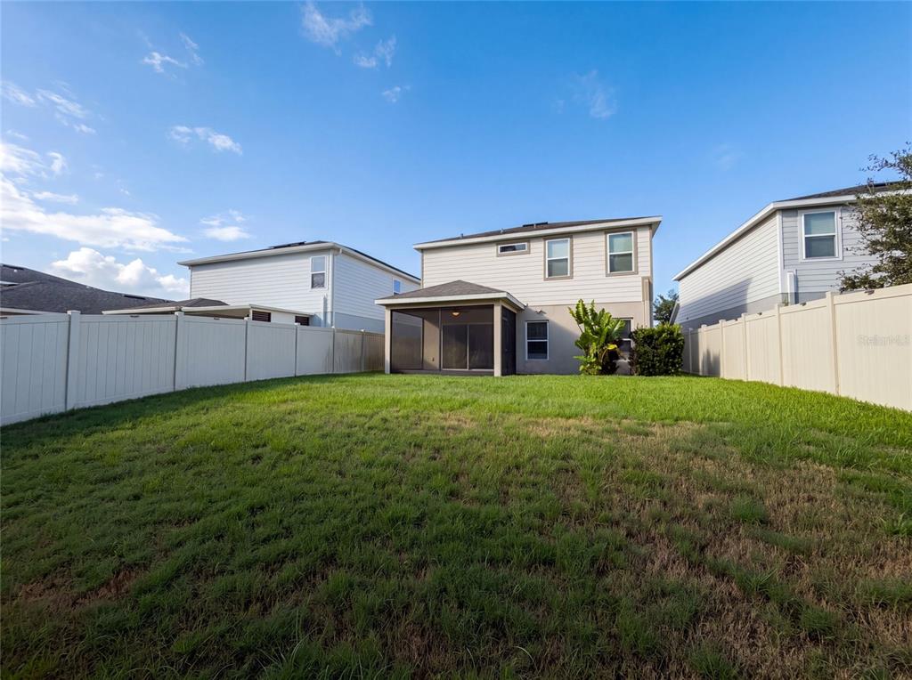 The backyard of a two-story house features a screened-in patio and a white vinyl fence — 10654 HAWKS LANDING DRIVE, LAND O LAKES, FL