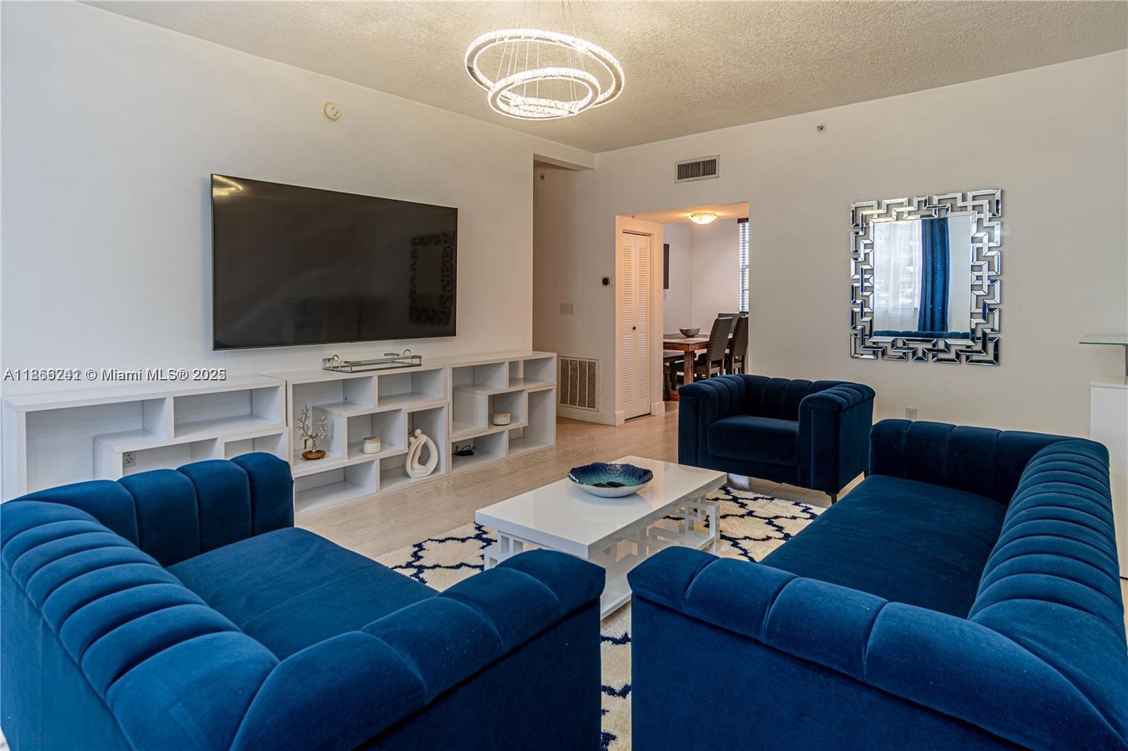 A living room features blue velvet furniture, a white media console, and a modern chandelier — 2069 S Ocean Dr, Hallandale Beach FL 33009, HALLANDALE BEACH, FL